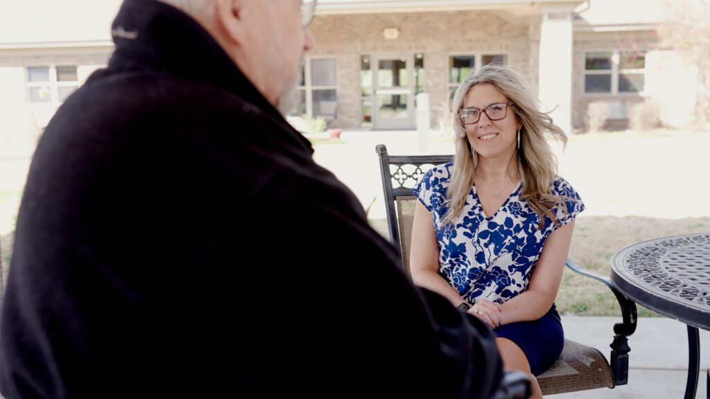 A woman smiles at a resident at a skilled nursing facility